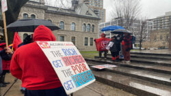 ACORN members present testimonies on the steps of the Human Rights Monument surrounded by protest signage