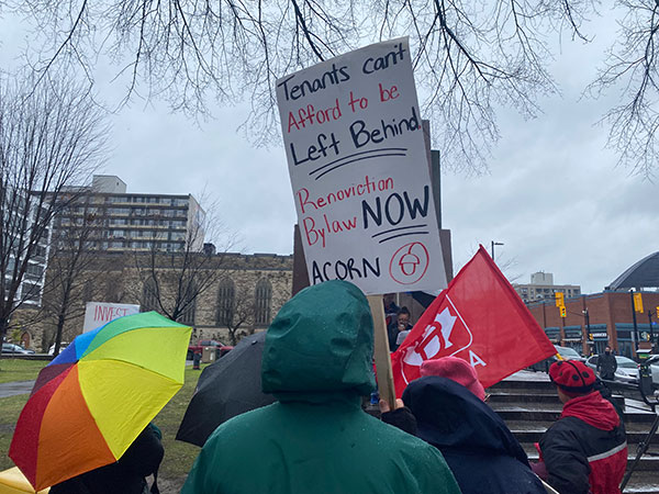 A sign at the rally reads "Tenants can't afford to be left behind renoviction bylaw NOW ACORN"