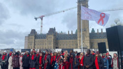 Members of the AIDS Committee of Ottawa and other organizations stand at the bottom of the World AIDS Day flag on Parliament Hill