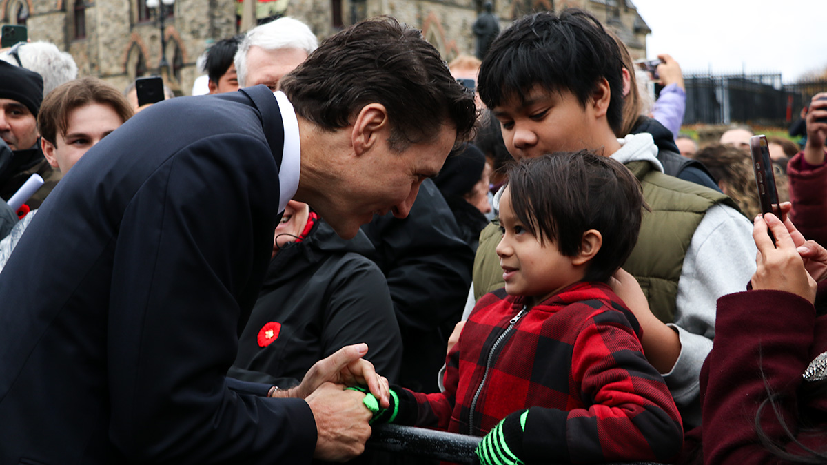 Prime Minister Justin Trudeau shakes hands with a child in a crowd at the National Remembrance Day Ceremony. 