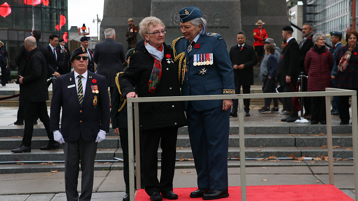 National Silver Cross Mother Maureen Anderson (left) and Gov. Gen. Mary Simon (right) stand on a podium in front of the National War Memorial. 