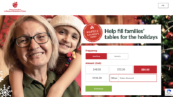 An older woman smiles at the screen as a child leans on her shoulders and smiles wearing a santa hat. In the background is a Christmas tree and christmas decorations. To the right of the woman and child is a digital pop up reading, "Help fill families' table for the holiday."