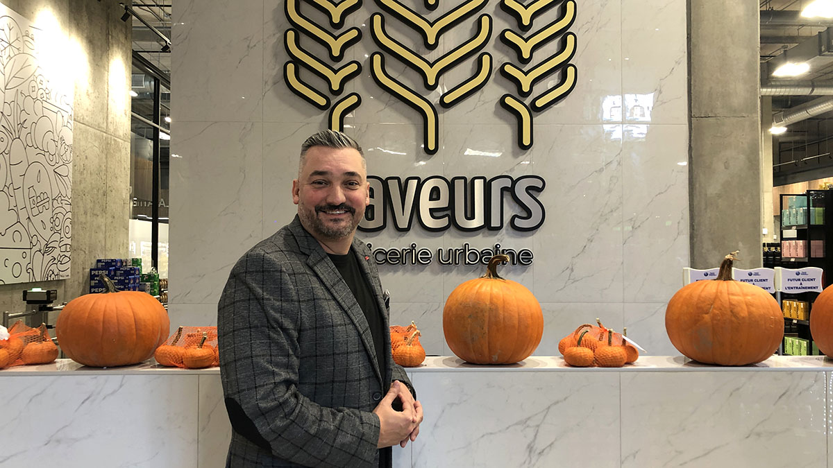 Dany Plante, the founder of Saveurs - Épicerie urbaine standing in front of the store sign. 