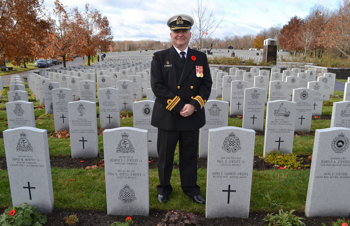 An officer looks stands among headstones in a military cemetery, looking at the viewer.