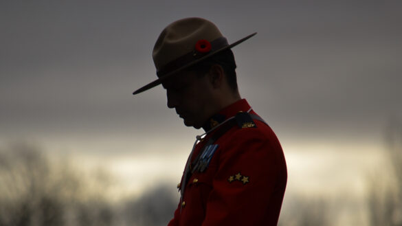 A RCMP officer stands with his head tilted down at a Remembrance Day ceremony.