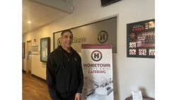 Tasso Vasilas, the Owner of Hometown Sports Grill in front of a poster