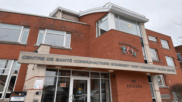 A red-brick multi-storey building with an overhead sign heading "Somerset West Community Health Centre." A logo with four colourful people figures under a grey arch sits above the heading.