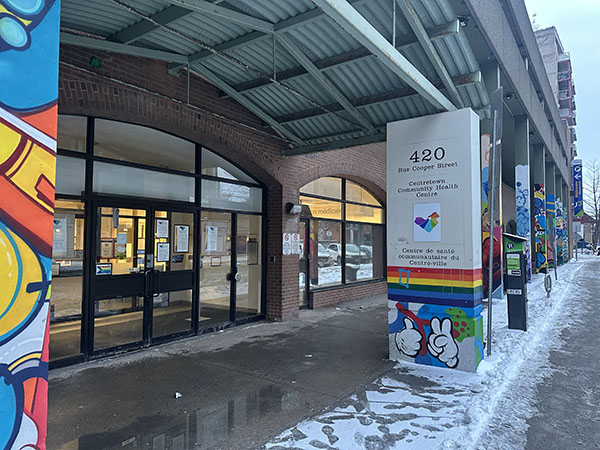 Automatic doors to a community health centre to the left with a colourful post which says 420 Copper Street, Centretown Community Health Centre on it to the right. 