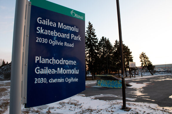 A park sign reads, Gailea Momolu Skateboard Park, infront of a skateboard park covered in snow.