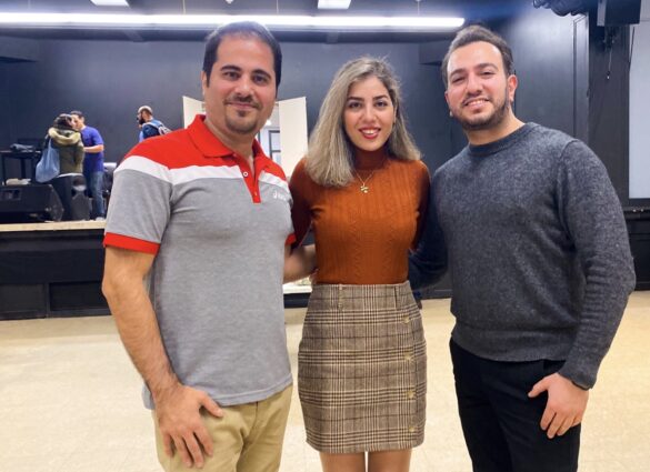 Two men and a woman stand together smiling in a public meeting hall