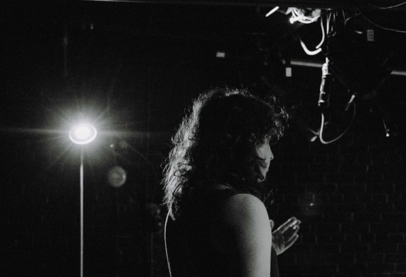 A person stands in front of a spotlight, photographed in black and white.