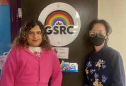 Two coordinators at Carleton's Gender and Sexuality Resource Centre pose at the centre's entrance with rainbow logo on door