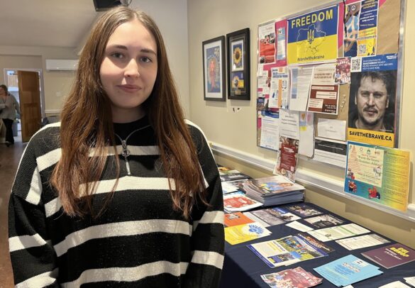 Young woman stands next to table and bulletin board with material supporting Ukraine newcomers