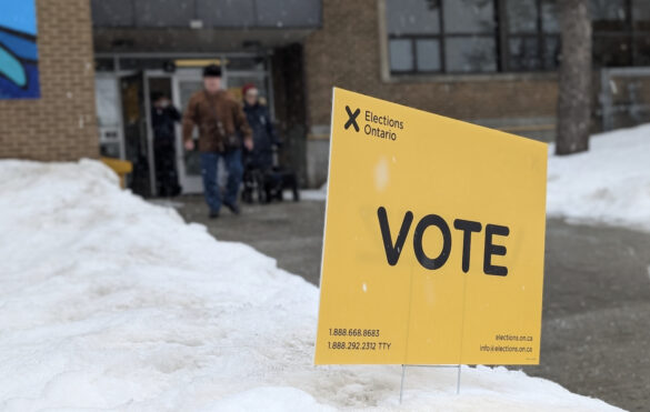 Elections Ontario sign in the foreground says VOTE as voters leave a polling station in Ottawa-Vanier riding.