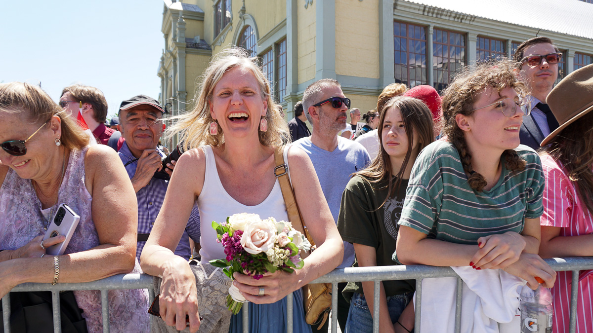 Woman with a bouquet stands in a crowd behind a barricade.