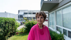 A woman stands on the lawn of an apartment building with a Tesla show room behind her.