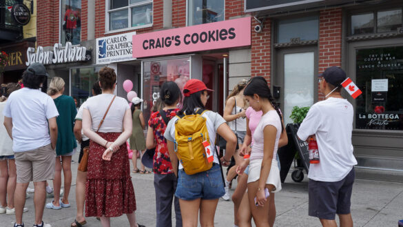 A crowd waits outside of a cookie shop.