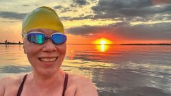 Swimmer Sarah Dobbin smiles in selfie with orange sunset behind her.