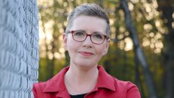 Mystery thriller author Katie Tallo stands in the center of the frame, smiling at the camera.