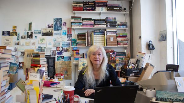 Dianne Savoy sits at the front desk of The Book Market surrounded by piles of books.