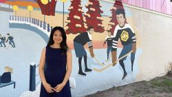 Irene Mei, owner of Fairy Dreams Bridal, stands in front of the "Chinese Aces Skate the Canal" mural.