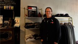 Geoff Cass, owner and founder of Red Bird Live, is standing and smiling in front of the merch at Red Bird Live.