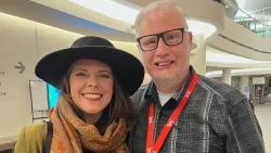 Melanie Brulée and Martin Noakes shoulder to shoulder at the 2025 Canadian Folk Music Awards. Brûlée wears a large brimmed black hat (her signature). They both smile ear to ear with their red passes for the event at the Canadian Museum of History in Gatineau Qc. [Photo courtesy of Great Dark Wonder]
